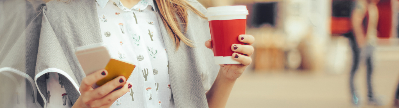 a woman holding her debit card, mobile phone, and a coffee